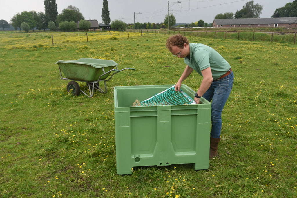 Bert van De Slowfeeder Specialist haalt het slowfeedernet uit een groene slowfeeder XXL in de weide