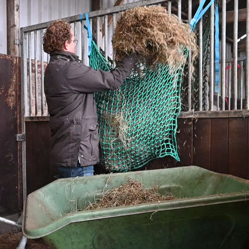 Bert van De Slowfeeder Specialist vult een slowfeeder hooinet in de stal