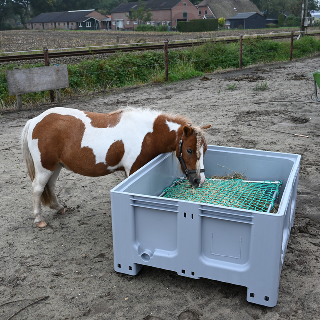 Grijze lage slowfeeder XXL gevuld met hooi, gebruikt door pony’s
