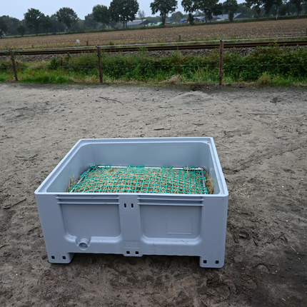 Grijze XXL slowfeeder met lage bak, gevuld met hooi voor pony’s