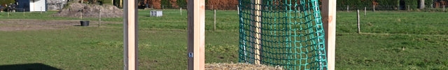 Houten slowfeeder hooihuisje met dak, hooibaal en groen hooinet staat leeg in de zonnige wei